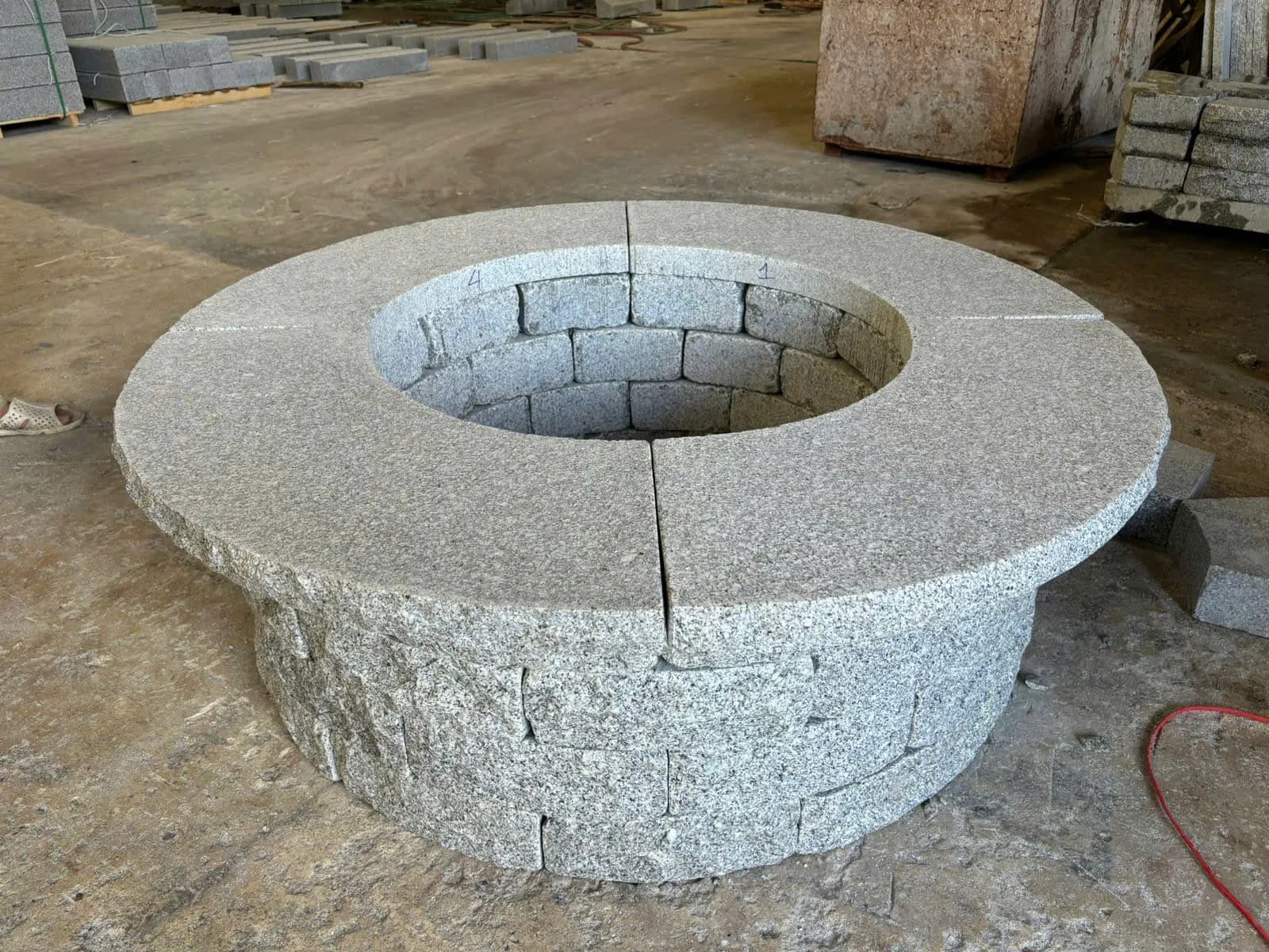 Round gray granite fire pit ring assembled on a workshop floor