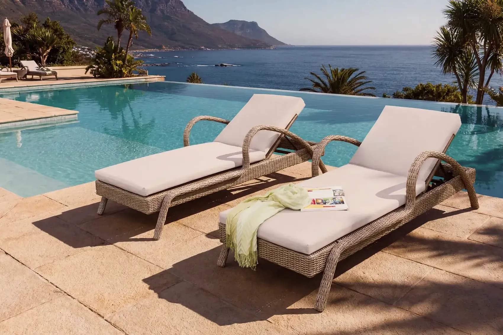 Two wicker sun loungers with cream cushions beside a pool