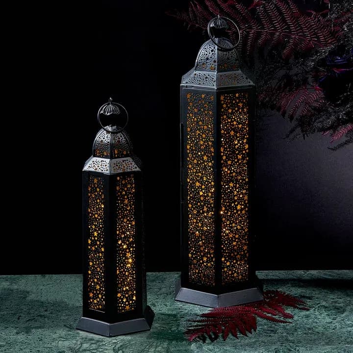 Two black metal lanterns with cut-out patterns lit from inside